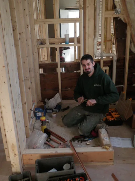 A Rock Coast technician soldering copper pipe in a framed-out room